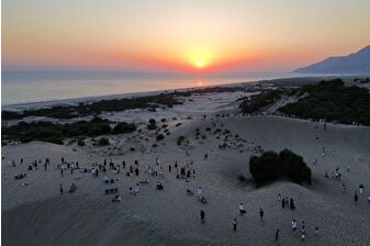 Patara'daki kum tepelerinde ziyaretçiler gün batımını izliyor