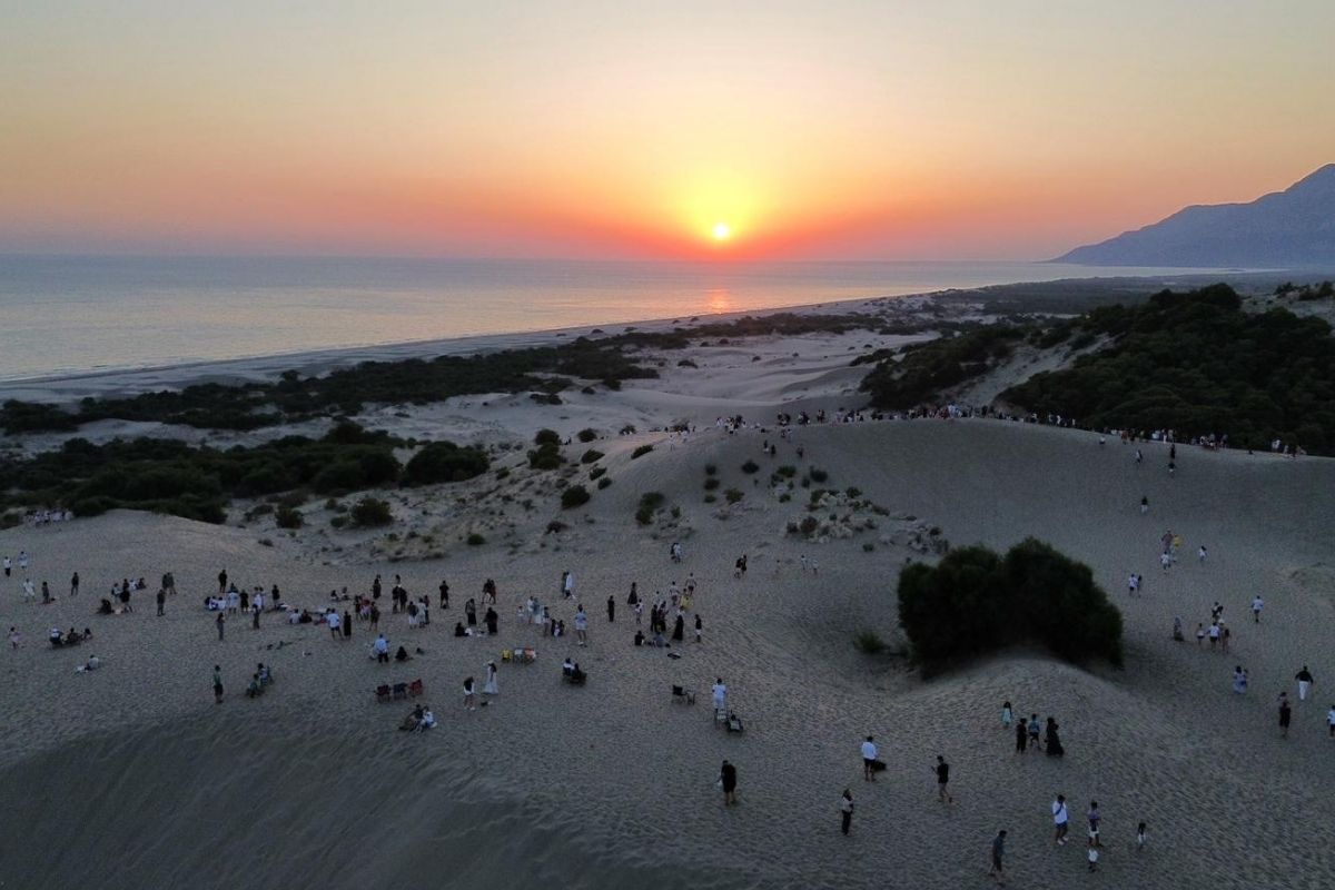 Patara'daki kum tepelerinde ziyaretçiler gün batımını izliyor